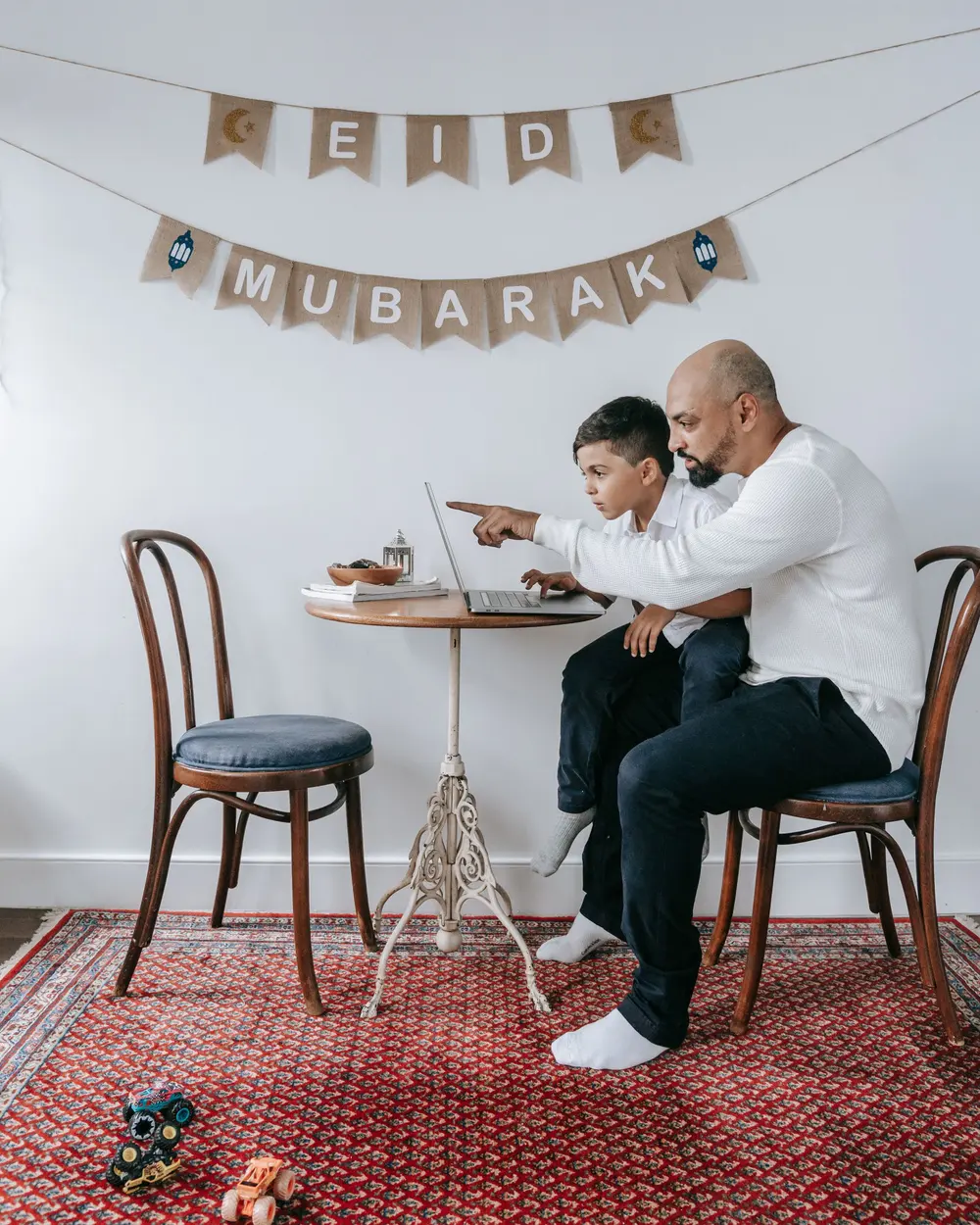 Un père et son fils devant un ordinateur portable, sous une guirlande de l'Aïd