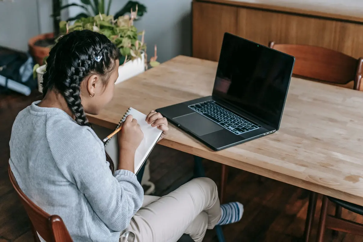 Une fillette, de dos, prend des notes à côté de son ordinateur portable